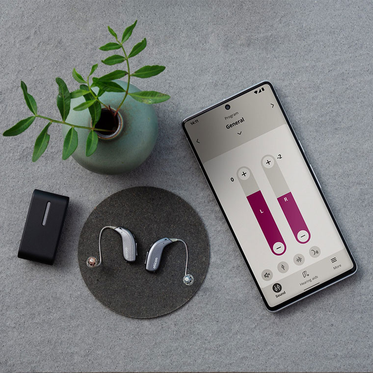 overhead shot of hearing aids next to a mobile displaying left and right volumes